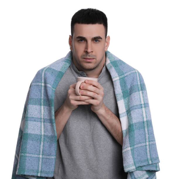 istock Man wrapped in blanket with cup of hot drink suffering from cold on white background 1449353885