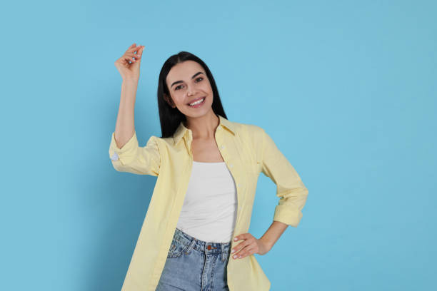 Young woman snapping fingers on light blue background. Space for text