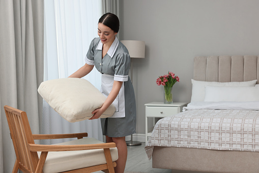 Young chambermaid cleaning up bedroom in hotel