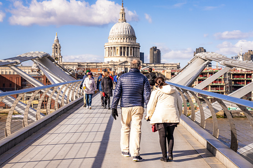 London, UK - People crossing the Millennium Footbridge over the Thames on a crisp day in March, with the dome of St Paul's Cathedral dominating the horizon.