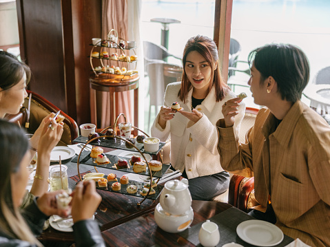 A half-body shot portrait of a group of female friends, young well-dressed elegant Asian adult women wearing Autumn or Winter clothes, eating cakes and dessert of an afternoon tea set, enjoying the delicious tasty food together, while talking or chatting to each other, in a luxurious hotel room. They are looking at each other.

Four young Asian girls enjoying their day and hanging out in a luxurious hotel indoors while relaxing during holiday or vacation.