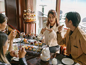 Young happy Asian women female friends eating cakes and dessert for afternoon tea in luxurious hotel or cafe indoors in daytime