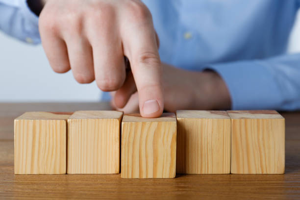 istock Man arranging empty cubes in row on wooden table, closeup. Space for text 1449355842