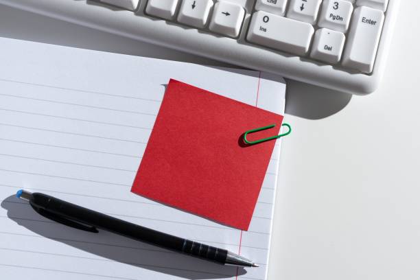 Sticky Note With Important Idea Clipped On Opened Notebook On Desk With Pen