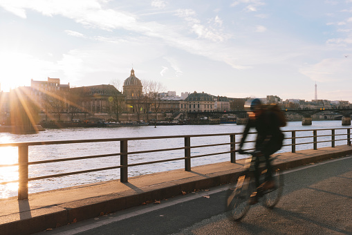 Unrecognisable man ridding bicycle along Seine river during sunset in Paris France