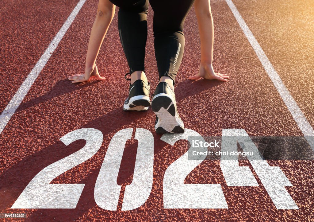 Rear view of a woman preparing to start on an athletics track engraved with the year 2024 2024 Stock Photo