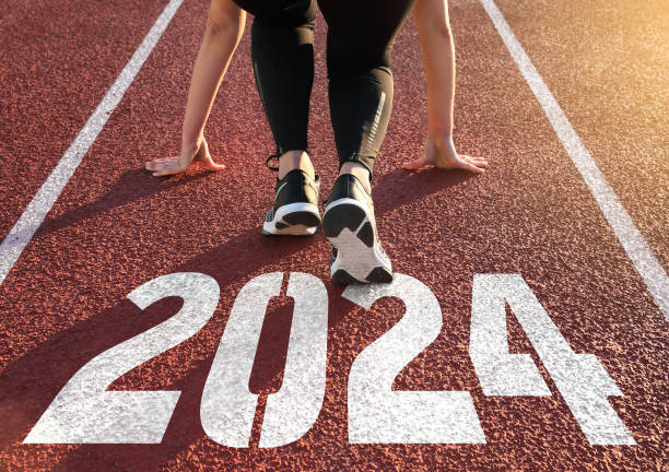 2024 Rear view of a woman preparing to start on an athletics track engraved with the year 2024 starting line stock pictures, royalty-free photos & images