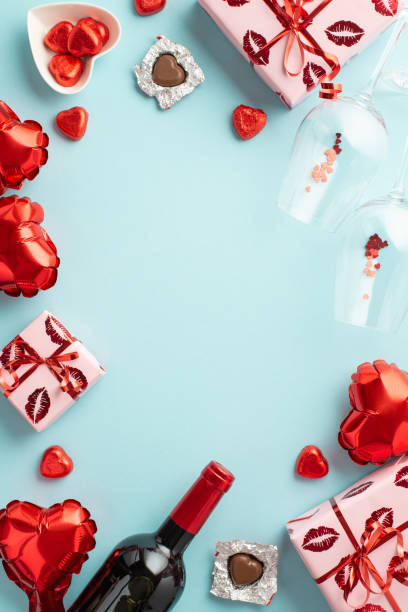 widok z góry: pionowe zdjęcie pudełek upominkowych balony w kształcie serca, kieliszki do butelek wina, konfetti i spodek z cukierkami na izolowanym pastelowym niebieskim tle z pustą przestrzenią pośrodku - valentines day candy chocolate candy heart shape zdjęcia i obrazy z banku zdjęć