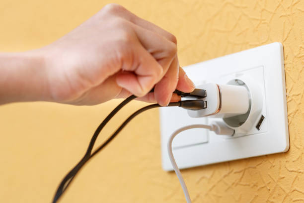 istock Hand plugs in black cord into usb charger pluged into white electric plug with built in usb ports. 1449369141