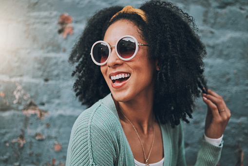 Fashion, summer and black woman in city with beauty, sunglasses and smile by blue brick wall. Travel, adventure and girl with trendy outfit having fun on weekend, holiday and vacation in urban town