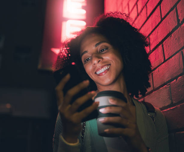 Happy black woman, phone and neon lights building in city night out, social media and online web location search. Young girl smile, mobile communication and 5g tech streaming on smartphone in town mujer feliz, teléfono y café en la ciudad por la noche mediante la construcción de luces de neón, redes sociales y búsqueda de ubicación web en línea. sonrisa de niña, comunicación móvil y transmisión de tecnología 5g en teléfonos inteligentes