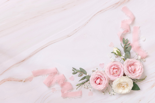 Pink and cream roses and silk ribbons on white marble top view. Romantic flat lay with pastel flowers. Wedding, Valentines, Spring or Mothers day concept