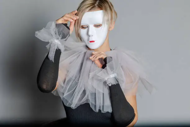 Woman in white theater mask and harlequin collar on gray background. Fancy dress, masquerade clothes