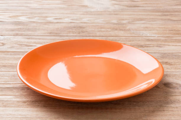 istock Perspective view of empty orange plate on wooden background. Empty space for your design 1449382692