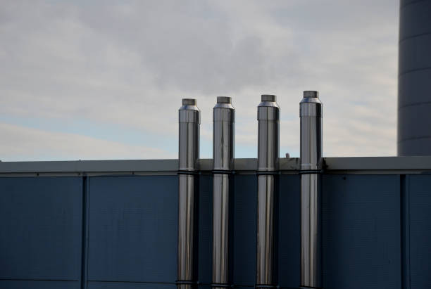 Industrial white building with sheet metal facade of repeating rectangle paneling. on wall are two silver-shiny chimney pipes with a curved and bevelled stainless steel pipe. gas heating turbo boiler edificio industrial blanco con fachada de chapa metálica de revestimiento rectangular repetitivo. en la pared hay dos tubos de chimenea plateados brillantes con un tubo de acero inoxidable curvo y biselado. caldera turbo de calefacción de gas