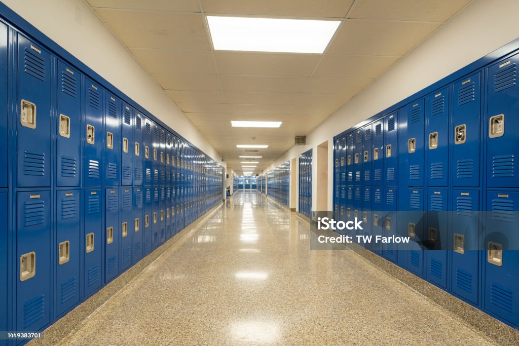 Typical, nondescript USA empty school hallway with royal blue metal lockers along both sides of the hallway. School Building Stock Photo