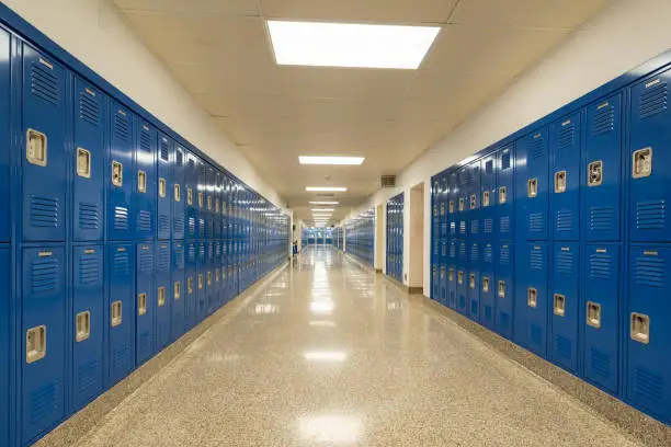 Typical, nondescript USA empty school hallway with royal blue metal lockers along both sides of the hallway.