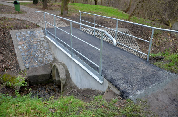 istock newly renovated bridge in the park over a small stream. concrete structures with a pipe passing through the flow lines. asphalt surface, metal sheet zinc drip tray. pipe railings, lawn, garden, cycle 1449385185