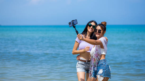 vacanze vacanza vacanza estiva. selfie sulla spiaggia. femmina asiatica e donna caucaca abbracciano e baciano sulla spiaggia tropicale. - sensuality people mobile phone 30s foto e immagini stock