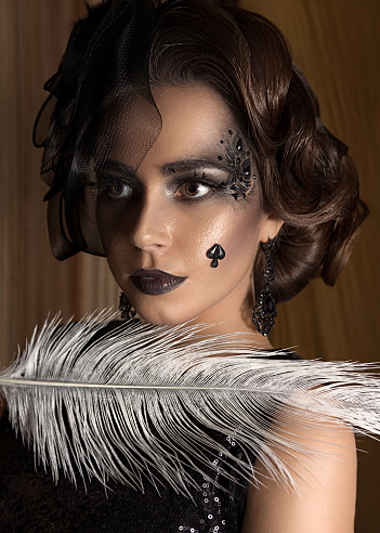 beautiful brunette woman in a hat and feathers in the dark. queen of spades. fashion art portrait