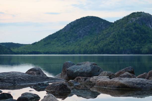istock Tranquil lake with stones in front of mountains covered with trees 1449386765
