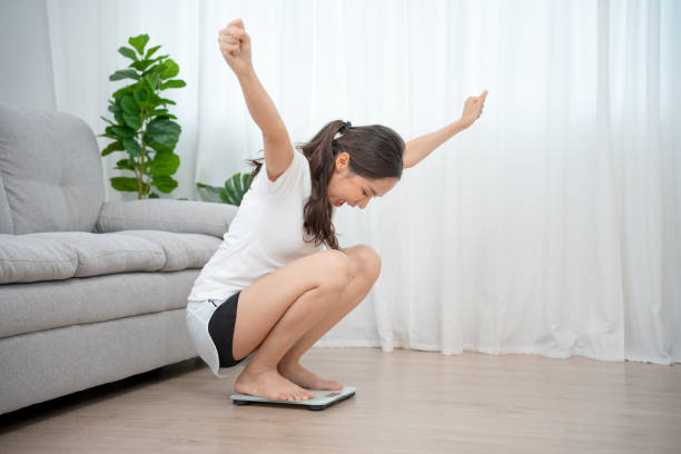 bien-être à la maison. régime, régime. femme sur une balance avec une expression de visage heureux. belle femme asiatique a réussi à perdre du poids après avoir rejoint un plan d’exercice et de régime avec un nutritionniste. - weight women medicine lost photos et images de collection