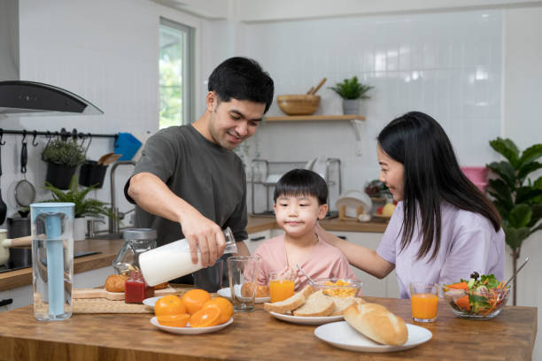 asian family breakfast at home. parents and children enjoy eating together, talking with laughter and good atmosphere. father and mother plays with son playfully at kitchen table. - domestic life young family family child imagens e fotografias de stock