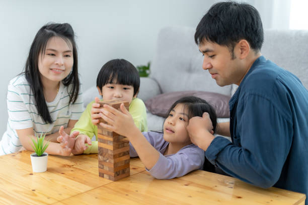 laughing and happy asian family on the sofa inside the house. father and mother play domino games with their adorable son and daughter. relaxing vacation and family happiness together - two parent family indoors home interior domestic kitchen imagens e fotografias de stock