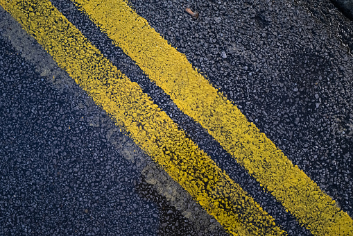 Abstract view of double yellow road markings seen on a wet tarmac road.