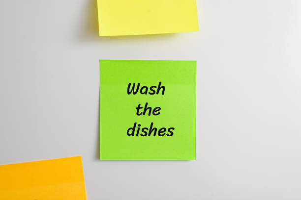 istock Self-adhesive sticker with reminder message Wash the dishes stuck on refrigerator in kitchen, close-up 1449395727