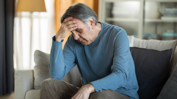 istock Old man holding his forehead sitting alone at home 1449398587