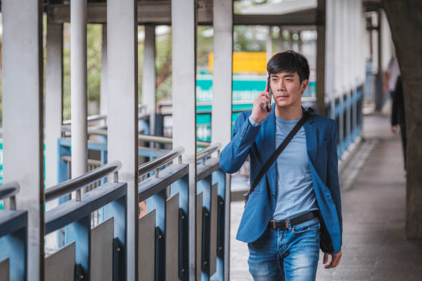 istock Businessman in suit using mobile phone and walking on skywalk at BTS sky train railway platform while traveling to work 1449401521