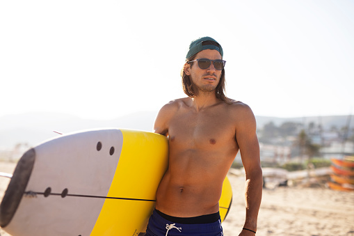Portrait of handsome surfer with his surfboard. Young man with a surfboard on the beach