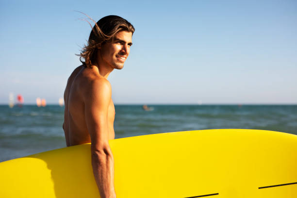istock Young man with a surfboard on the beach 1449403178