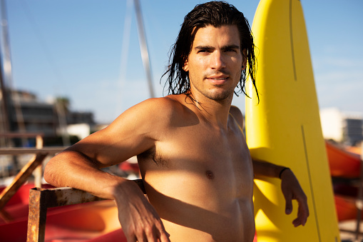 Portrait of handsome surfer with his surfboard. Young man with a surfboard on the beach