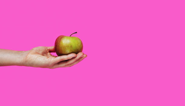 istock Fruit apple in hand against pink background with copy space. 1449403406