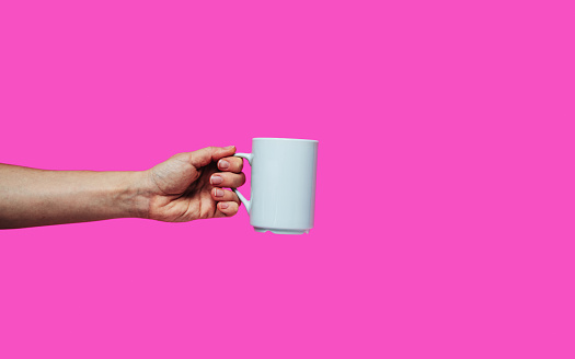 Isolated hand holds coffee mug against pink backdrop with space for text.