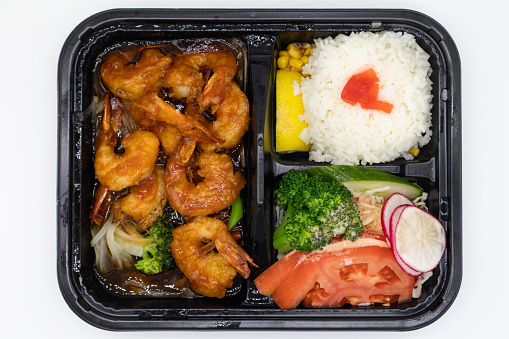 An overhead view of a delicious Japanese shrimp teriyaki bento box with white rice and vegetables on a white background