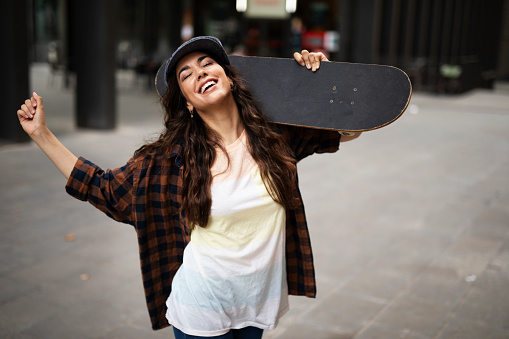 Portrait of young beautiful girl with skateboard. Happy smiling woman having fun outdoors