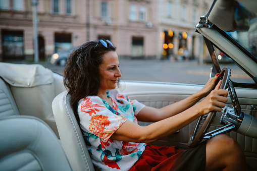 Womem going out to town in a vintage convertible car, having a relaxed weekend joyride.