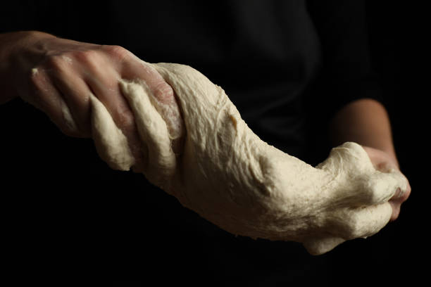 The cook stretches and kneads whole grain sourdough dough, selective focus.