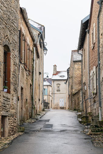 View along a narrow alley with old stone houses and snow-covered roofs. The small medieval village is classified as one of the most beautiful villages in France (plus beaux villages de France). The roofs are lightly covered with snow. 01/07/2022 - Flavigny-sur-Ozerain, Department Côte-d'Or, Burgundy-Franche-Comté, Arrondissement Montbard, France