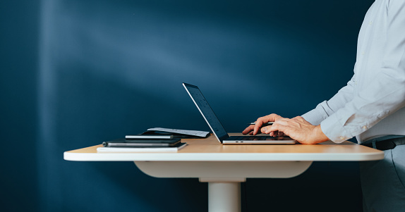 Close up photo of man hands typing business report on a laptop keyboard while standing at office desk.