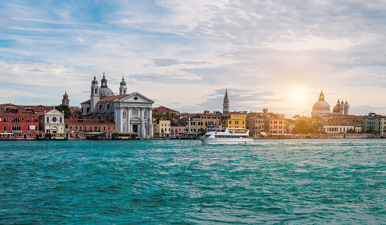 Wide image with buildings along the waterfront, Zattere quay with religious church in Dorsoduro neighbourhood. Sunset sky. Boat on the water. Travel concept Venice Italy.