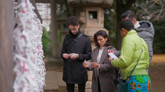 A group of multiracial friends are visiting a shrine and tying omikuji (fortune paper)