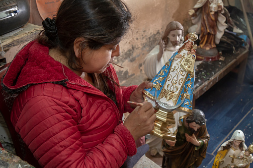 An ecuadorian female Artist repairing and retouching a Catholic statue of Virgin Mary on her studio before the Christmas Time, in Quito Historic Downtown near to Basilica and Convent of San Francisco.\n\nThe religion faith in Ecuador is very important and the people believe in their Saints for blessings.