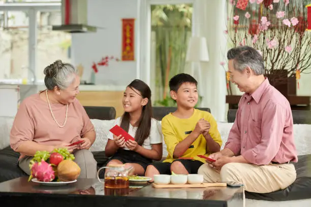Grandparents giving red lucky money envelopes to grandson and granddaughter