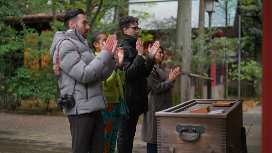A group of multiracial friends are visiting a shrine and praying.
