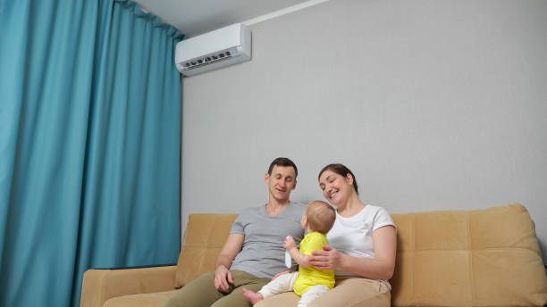 Family suffers from heat at home man turns on conditioner Family suffers from hot air in apartment and husband turns on conditioner to let cold stream in. Baby daughter sits and cries suffering from heat air conditioner family stock pictures, royalty-free photos & images