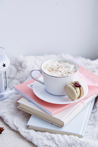 Aesthetics breakfast with hot drink with foam, delicate macaroon on the books. Sweet dessert at cozy home.